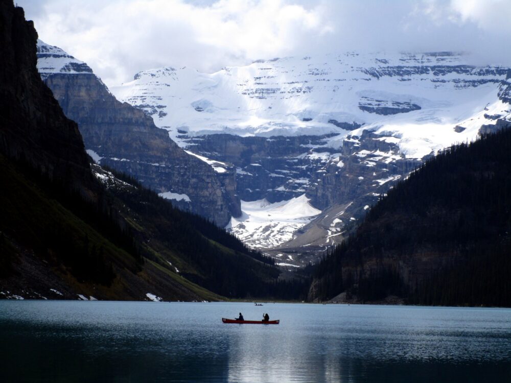 皮划艇的人在山湖上划桨，后面是雪峰