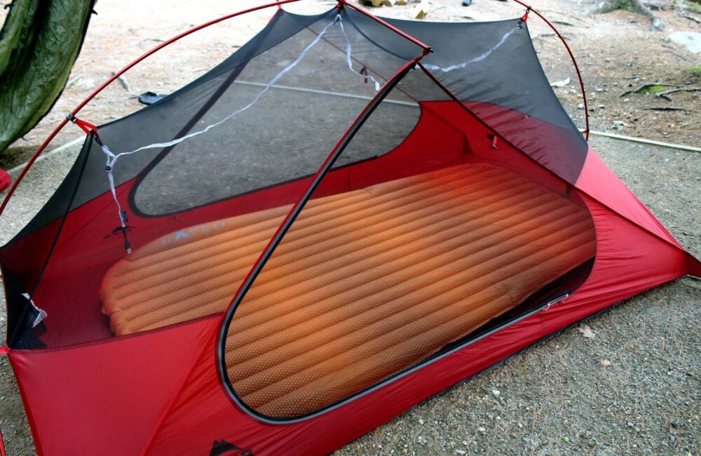 地上搭着红色小帐篷，透过网眼可以看到充气的橙色睡垫