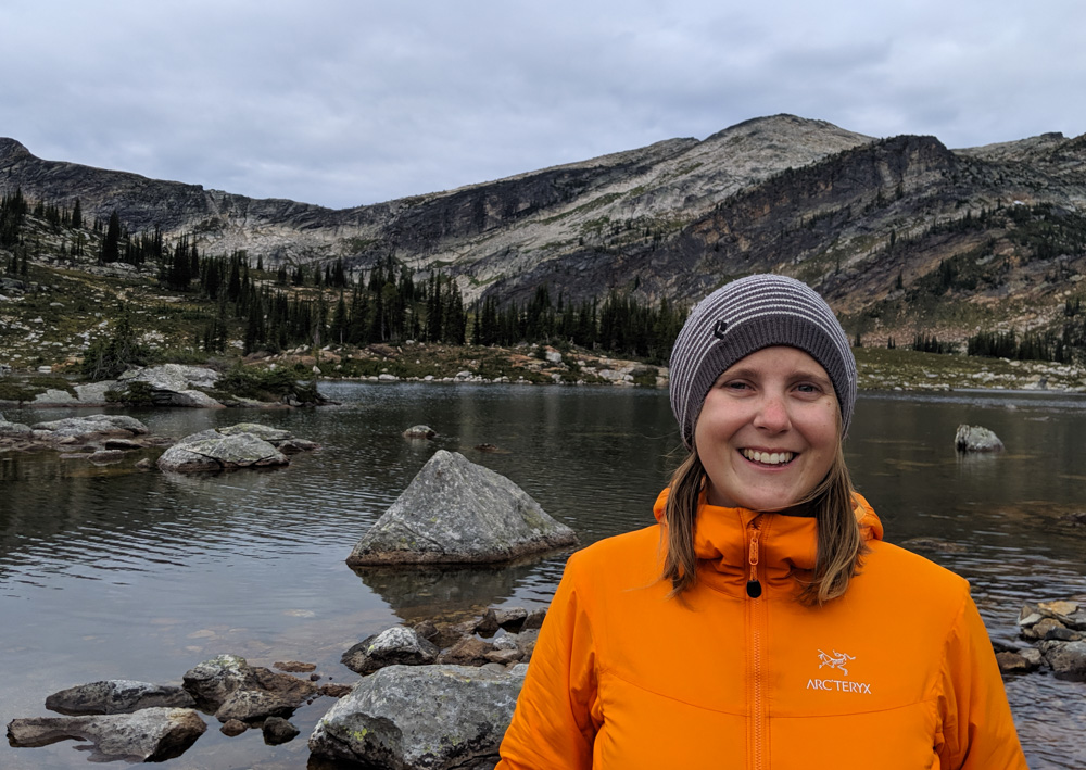 杰玛穿着橙色夹克和蓝白条纹羊毛帽子，在高山环境中直视镜头