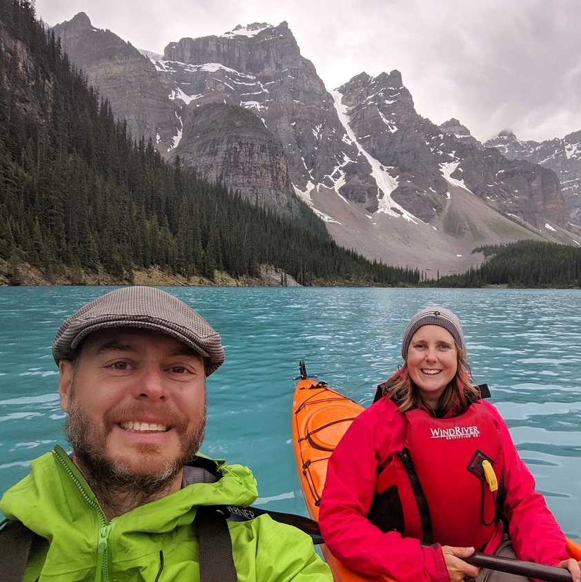 杰玛和jr在蓝绿色的冰碛湖上划着皮艇，后面有山