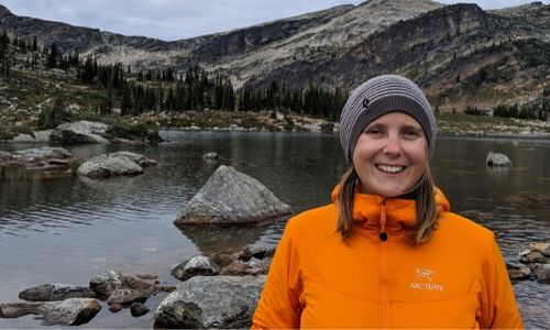 在高山湖前，穿着橙色夹克的杰玛看着相机