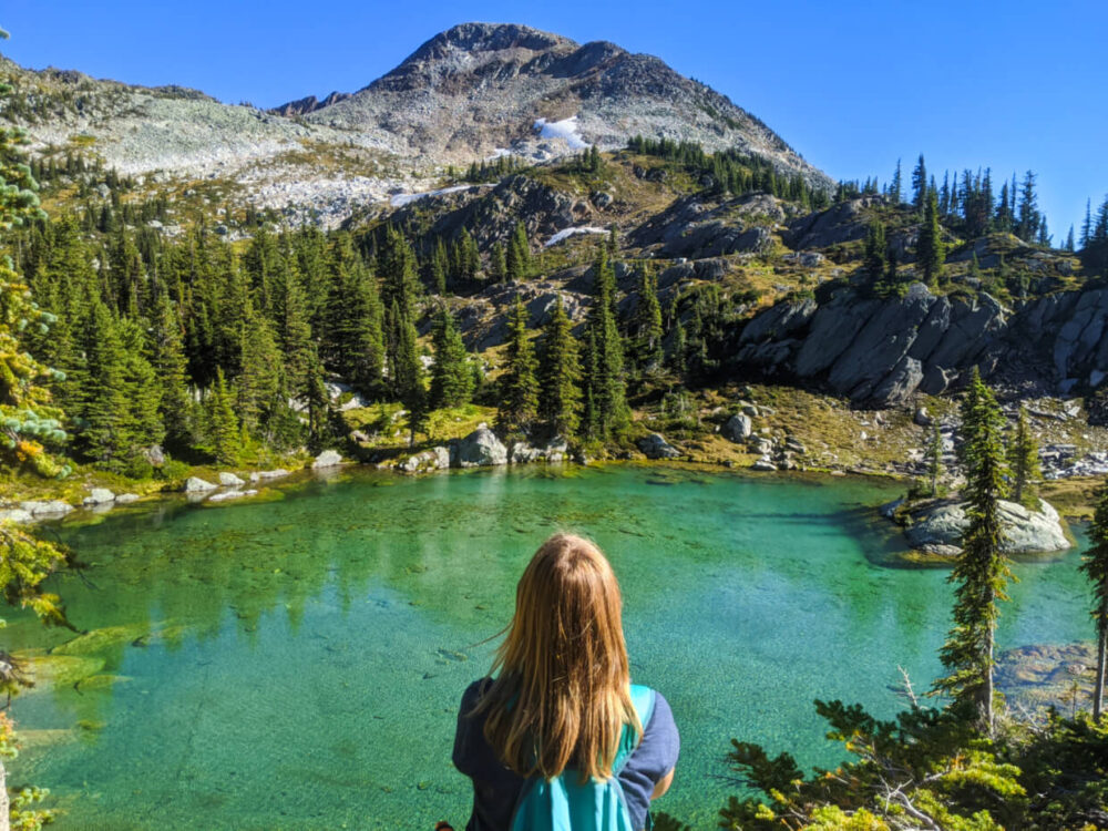 杰玛坐在绿松石色的湖前，湖的背景是山和山脊