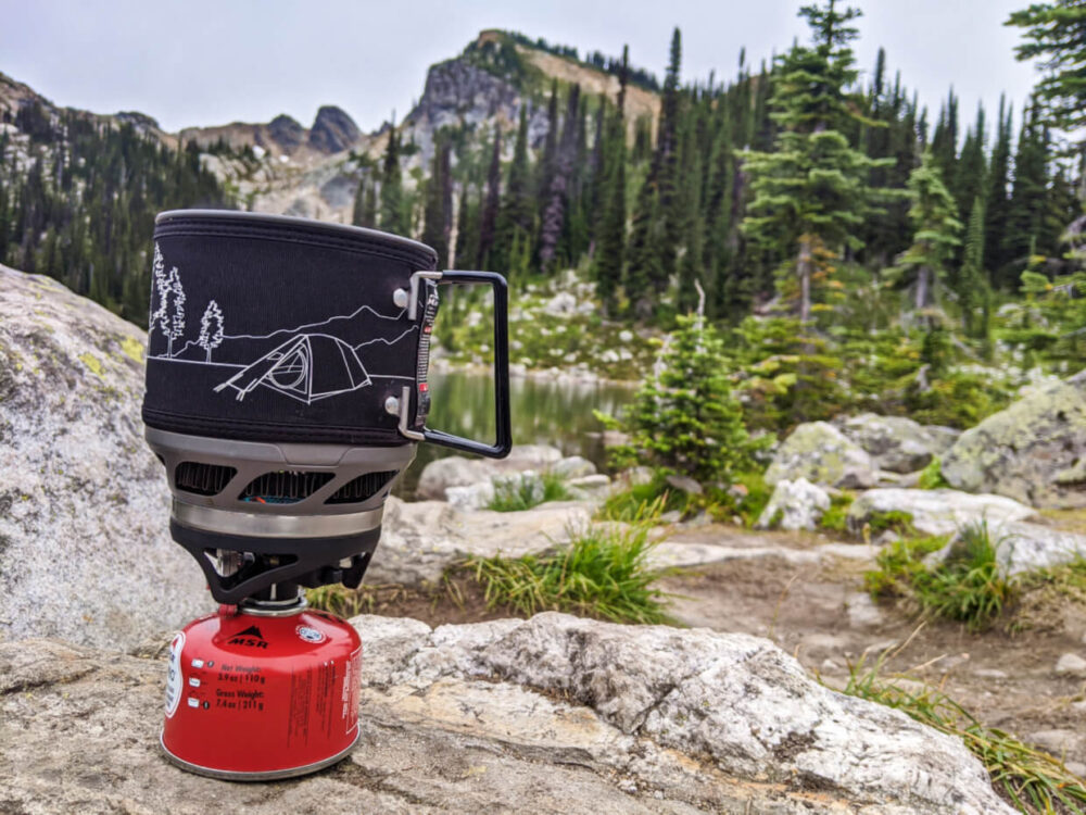 黑色和白色的野营炉上的红色煤气罐，放在一个岩石前面的山景