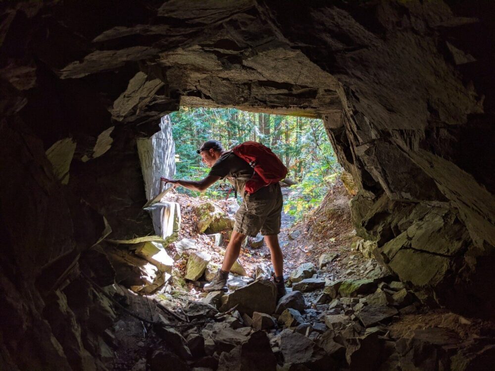 JR站在矿井入口处，看着外墙上的铭文。摄影师在岩石密布的矿井内向外眺望