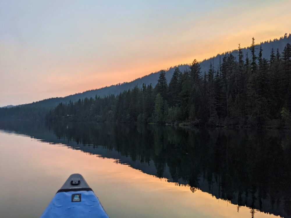 从独木舟上俯瞰宝石湖的日落景色，湖和森林的镜子般的倒影背后是橙色