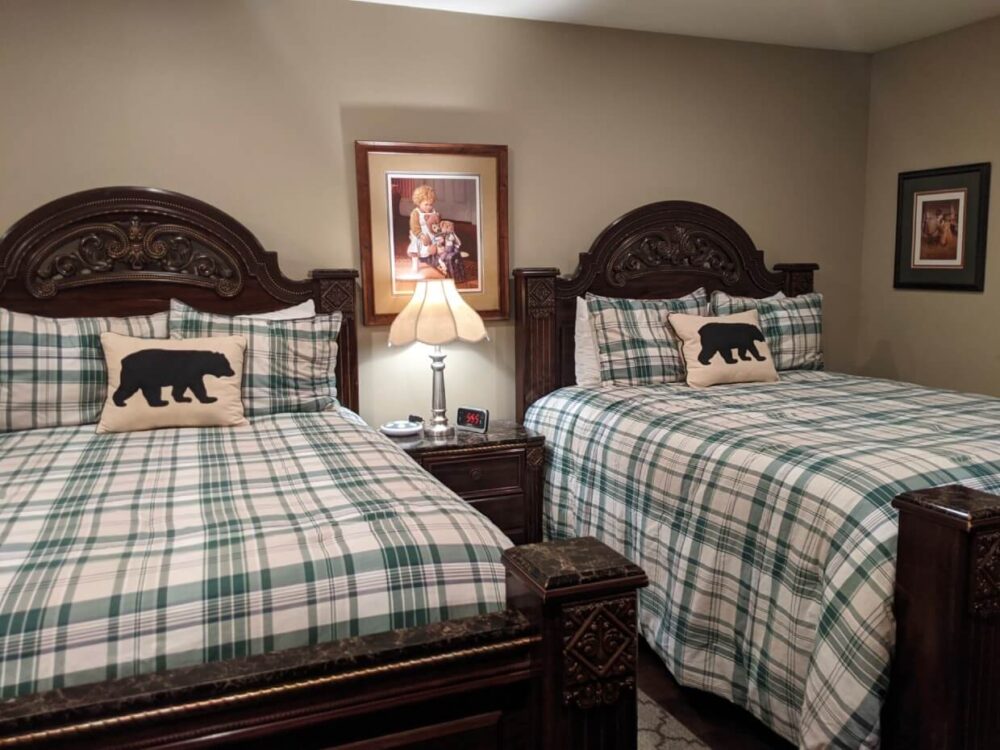 大福克斯Noble House Suites的两张双人床。床上有深色木框，格纹床单和带有熊图案的枕头