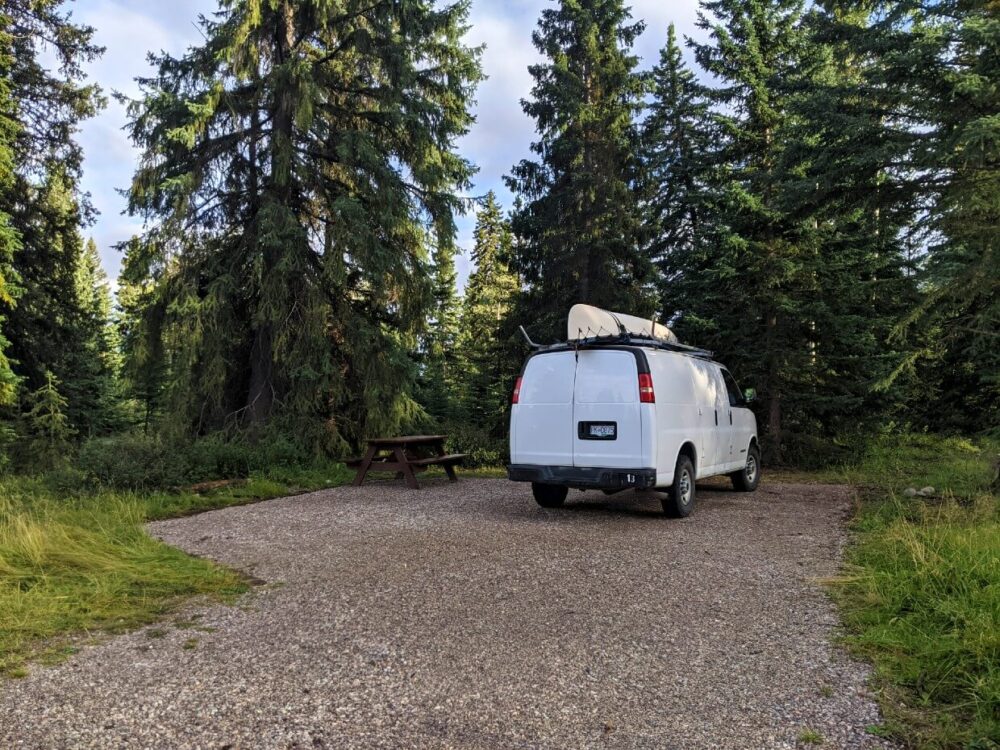 在惠斯勒露营地的砾石营地，白色货车停在野餐桌旁，周围是森林