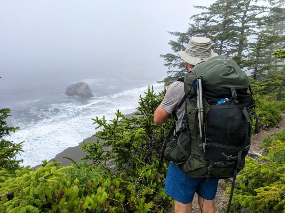 JR站在悬崖边的小道上，眺望雾蒙蒙的海景。他的背上背着一个大背包