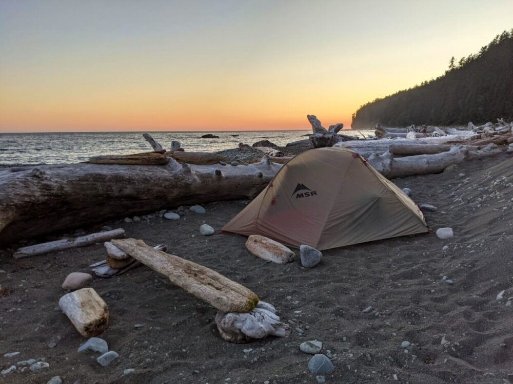 落日的颜色在天空后面在沙滩上搭起帐篷，被浮木包围