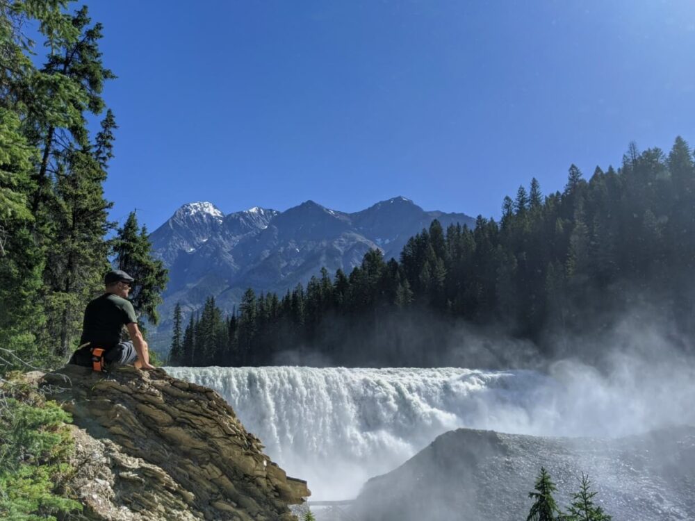 JR坐在宽阔的瓦普塔瀑布的左侧，瀑布的背景是群山