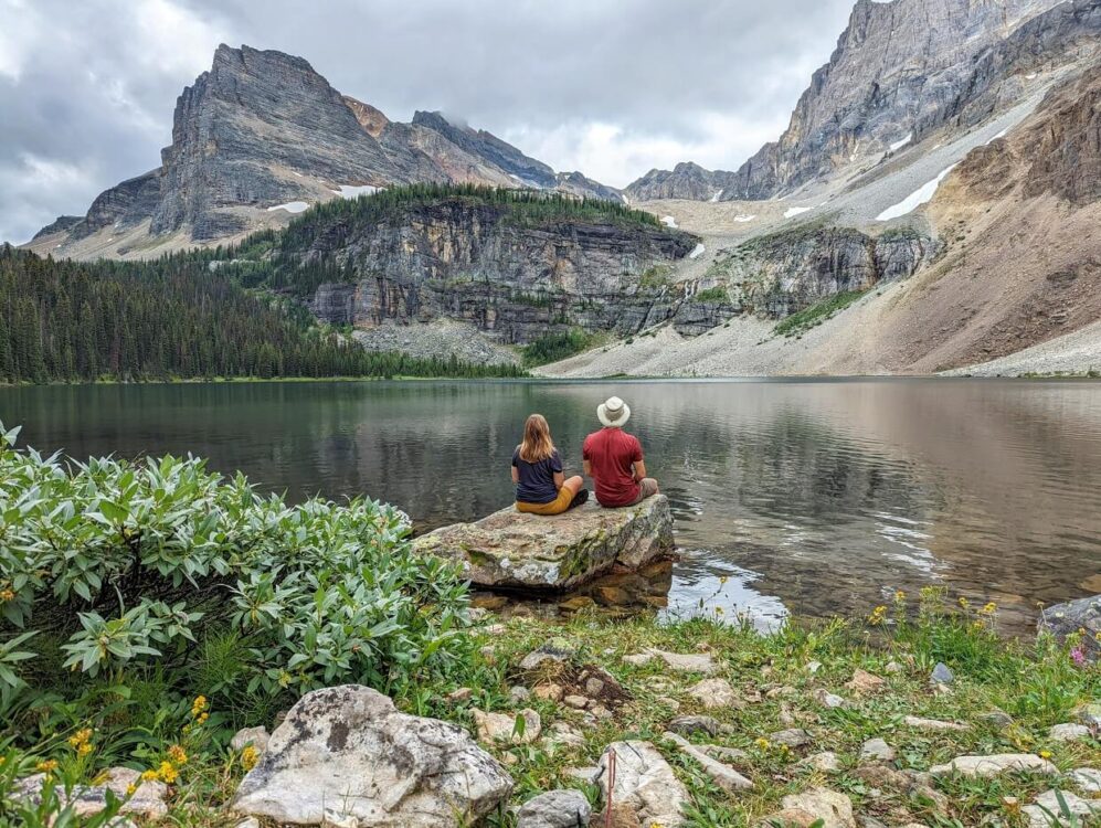 Gemma和JR坐在海督湖旁边的岩石上，非常平静，倒影着上面的山