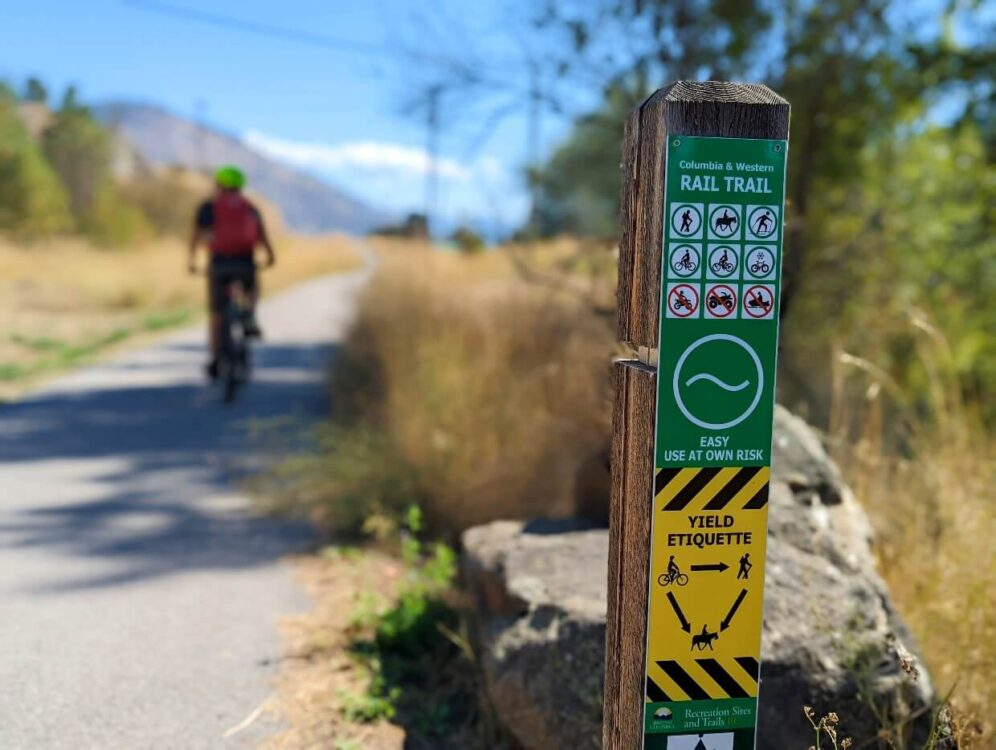 特写哥伦比亚和西部铁路的标志，JR骑自行车离开铺平的小道在背景